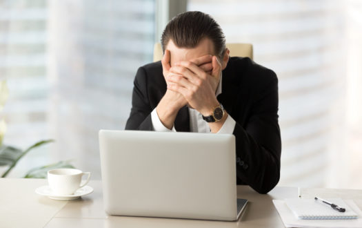 Terrified businessman covering face with hands in front of laptop.