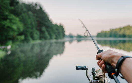 Fisherman with rod, spinning reel on the river bank. Sunrise. Fishing for pike, perch, carp. Fog against the backdrop of lake. background Misty morning. wild nature. The concept of a rural getaway.