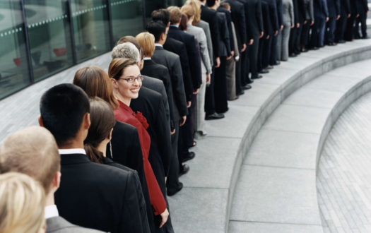 Businesswoman Standing Out in a Line of Business People Waiting Outdoors on a Step